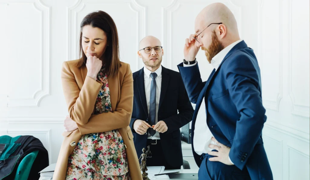 3 people in a room dressed professionally a divorcing couple standing with upset faces and lawyer standing behind them