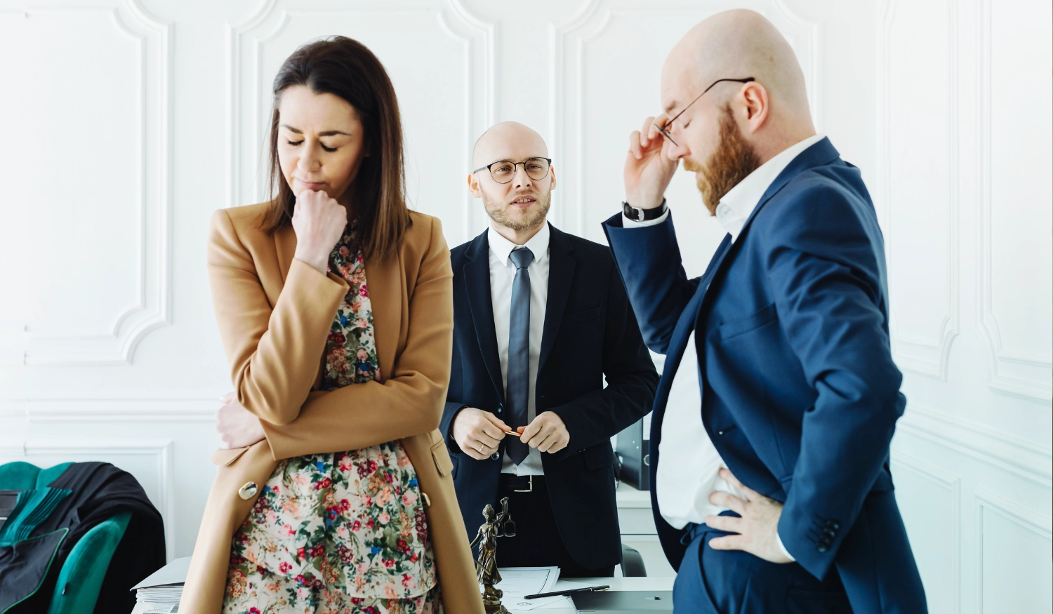 3 people in a room dressed professionally a divorcing couple standing with upset faces and lawyer standing behind them