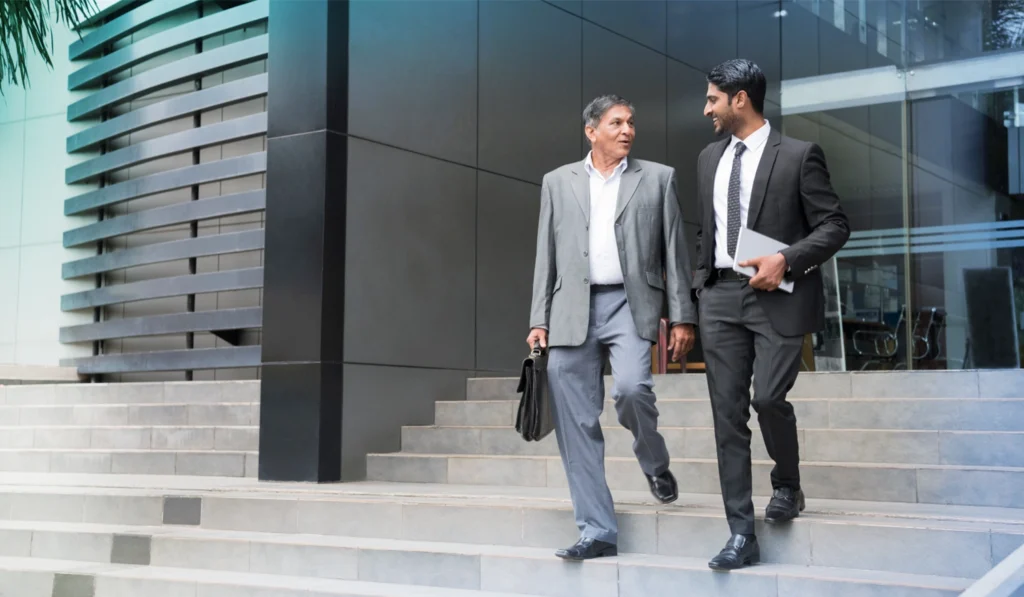 two men in business attire walking down steps outside of a building talking to eachother