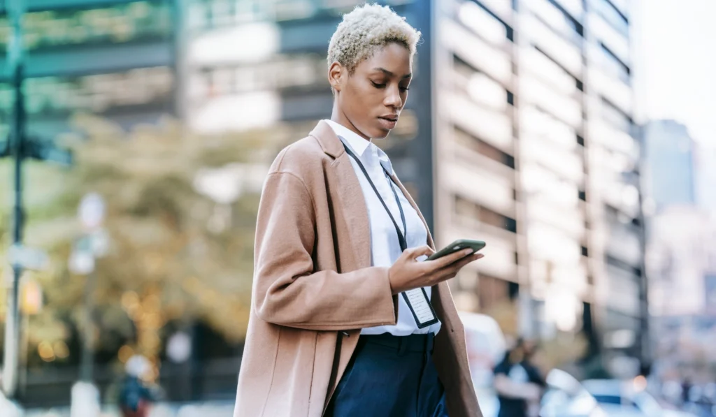 woman standing in city wearing professional attire looking at cell phone in hand