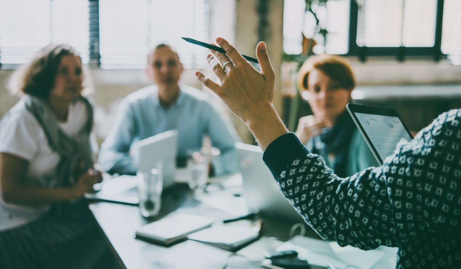 group of lawyers sitting at a desk listening to someone whose hand is in frame holding a pen