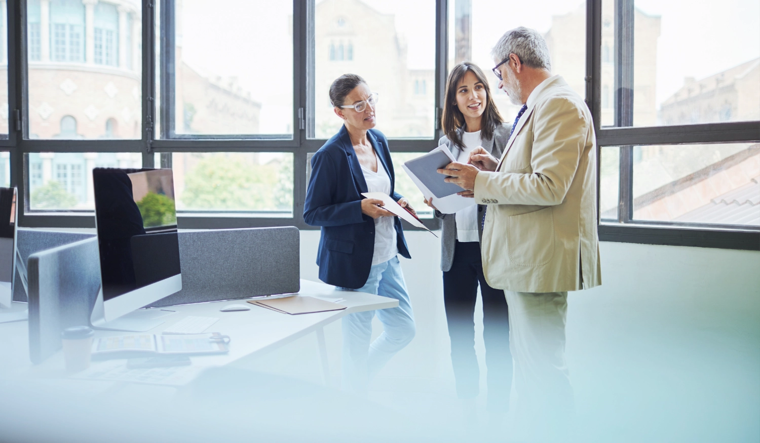 group of professional people standing in an office with floor to ceiling windows, discussing over a paper in one members hands